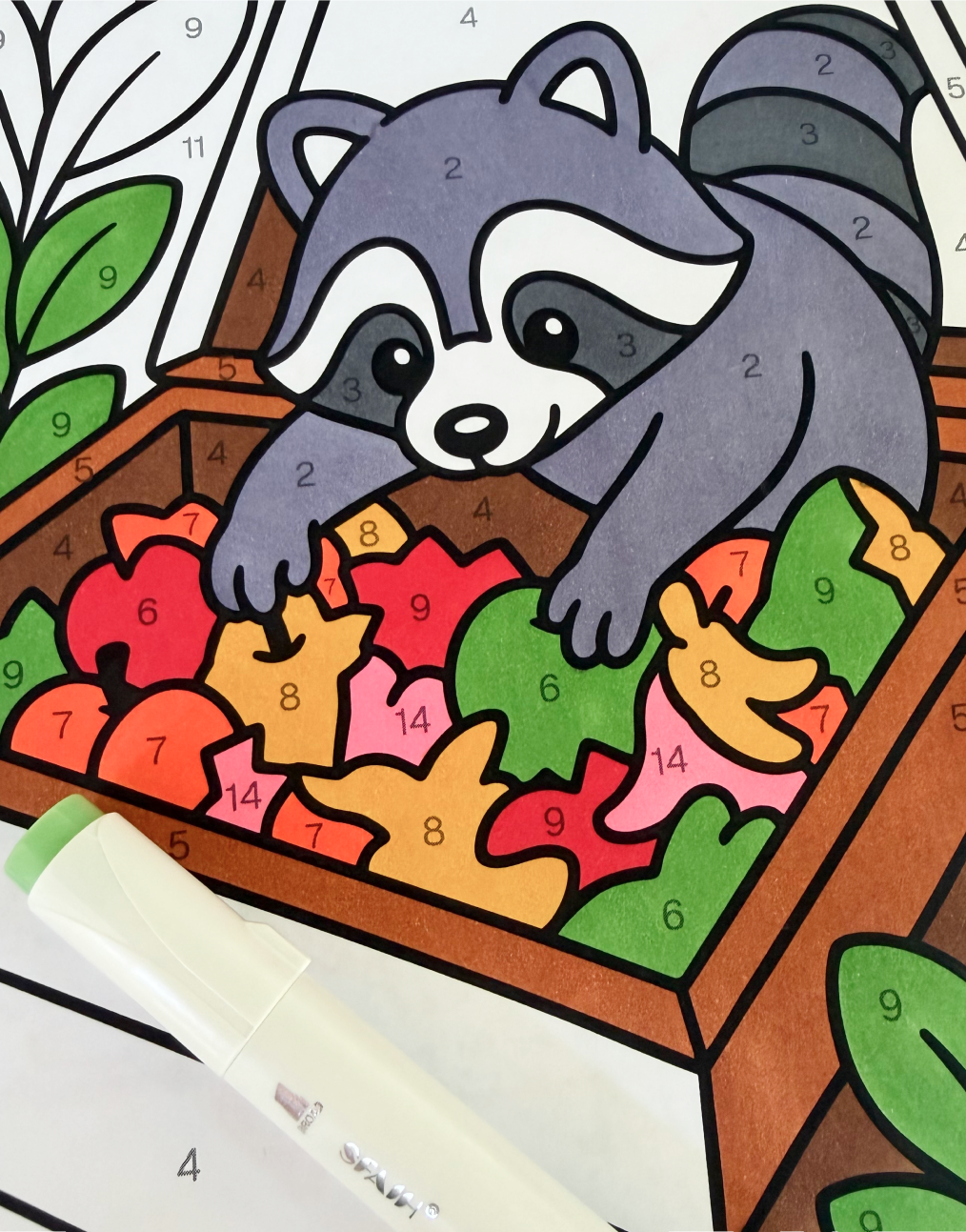 A color-by-number raccoon page part-way filled in, with an alcohol marker resting on top